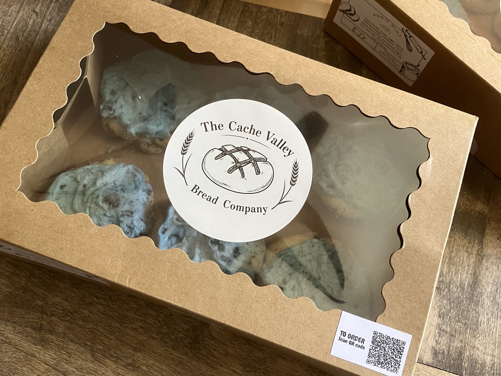 Aggie blue mint cookies in a windowed kraft box beside a wrapped loaf