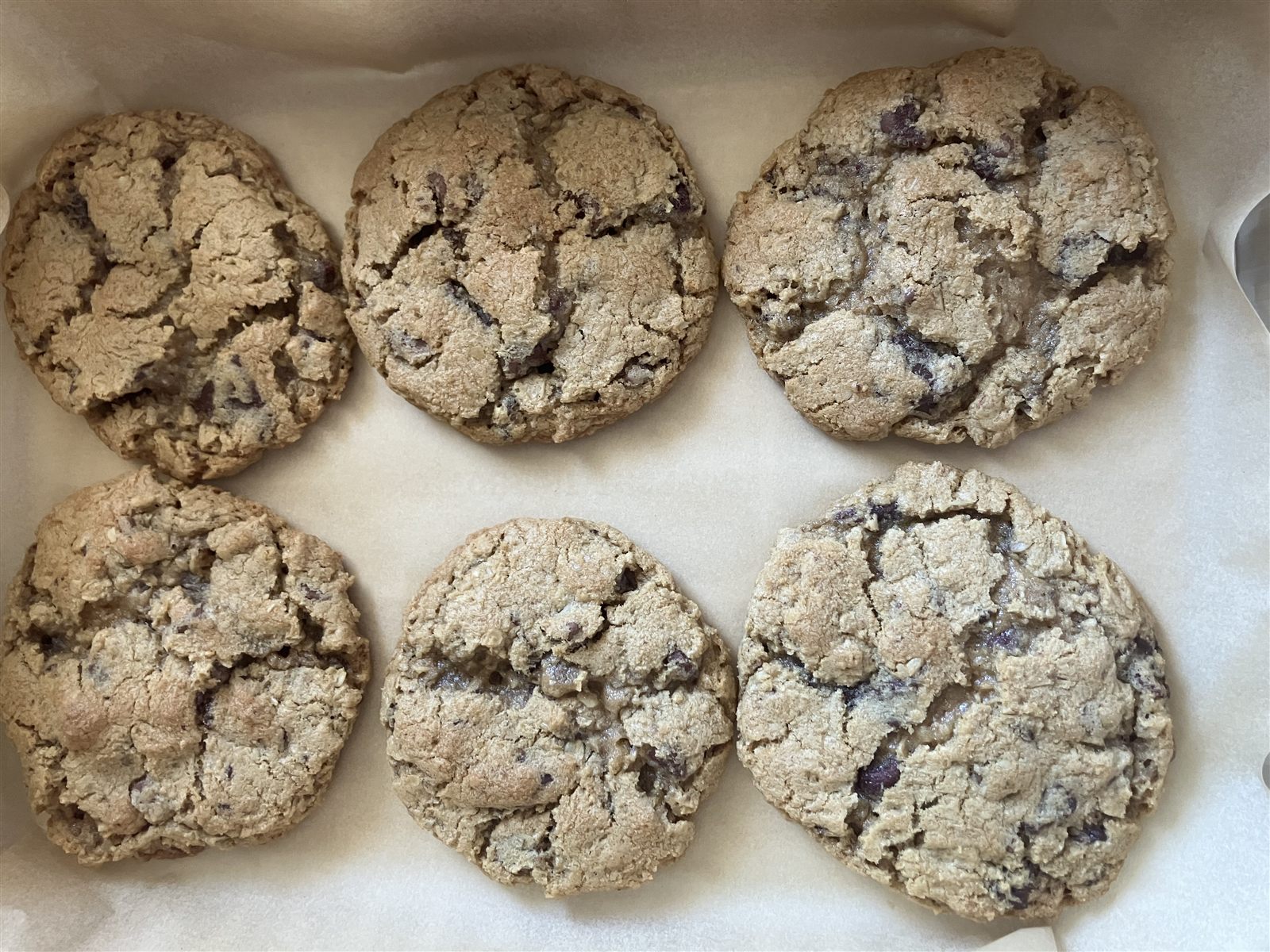 Six chocolate chip cookies on a parchment-lined baking tray