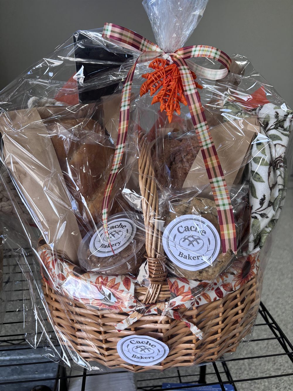 Autumn gift basket wrapped in cellophane with a plaid ribbon, holding breads, cookies and a seasonal throw