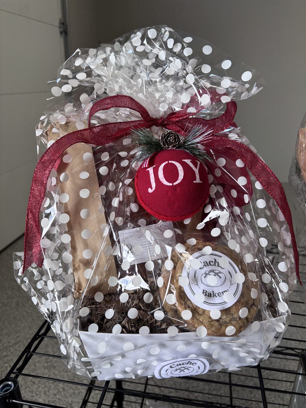 Holiday gift basket tied with red ribbon and a JOY ornament, holding sourdough and a chocolate chip cookie