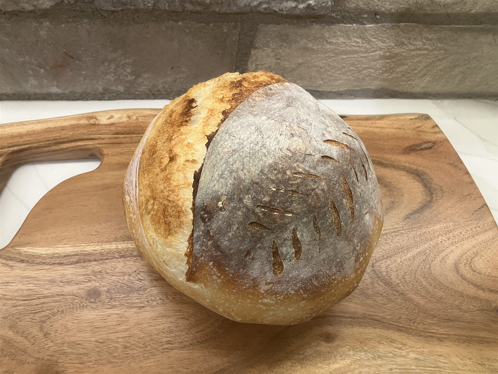 A round sourdough loaf scored with a wheat pattern on a wooden board